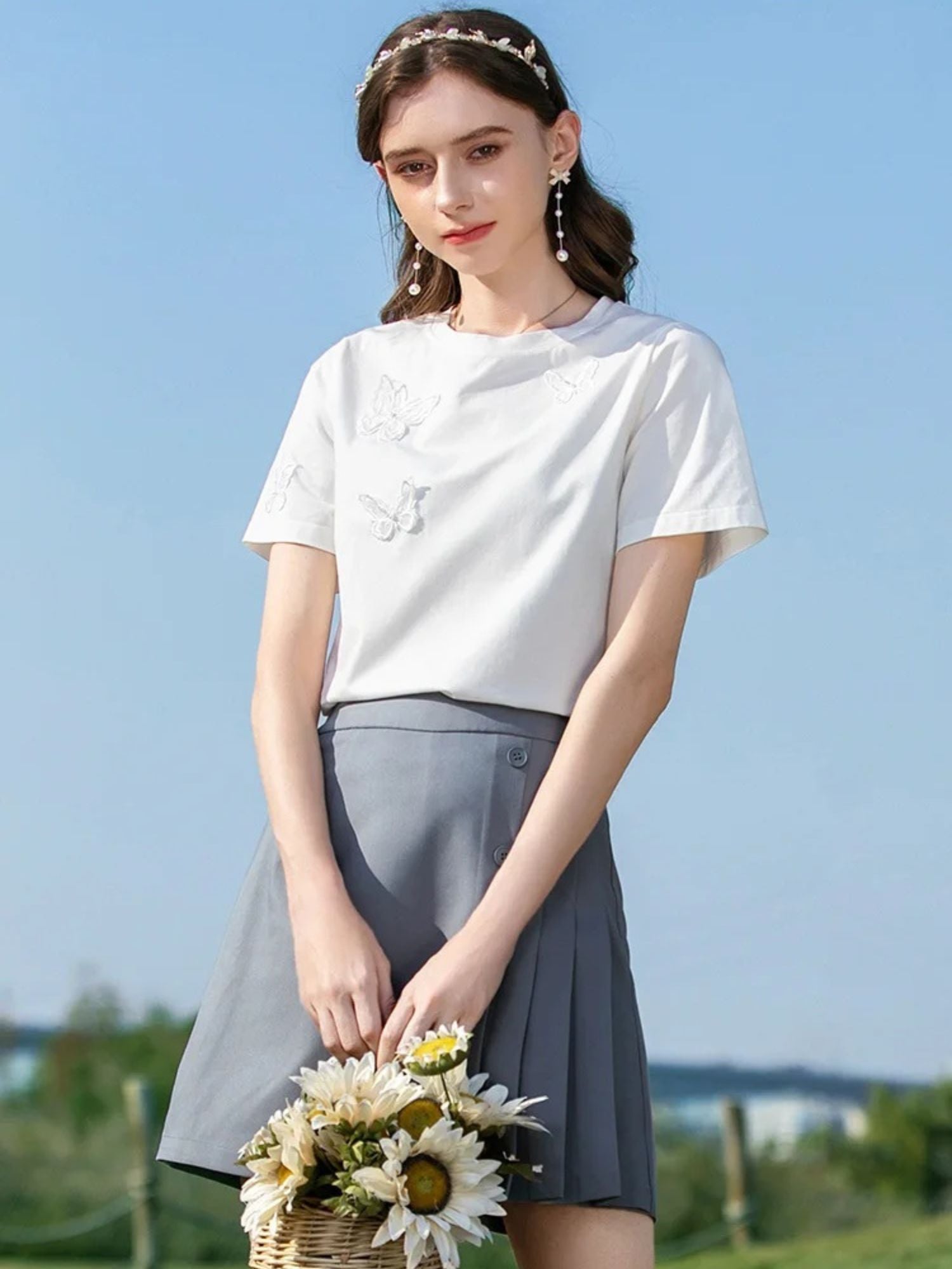 Woman in white butterfly top and gray skirt holding a small bouquet.
