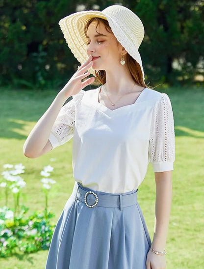 Woman in white embroidered blouse and blue skirt, laughing outdoors in sunlight.